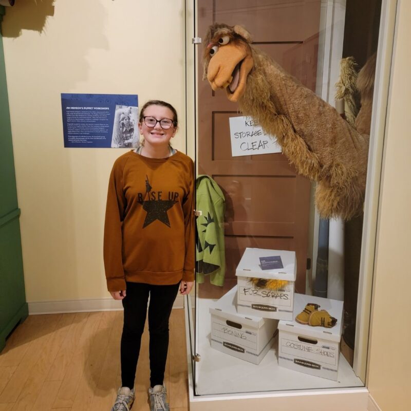 A teenage girl in a brown hoodie stands next to Sopwith the Camel from The Muppets.