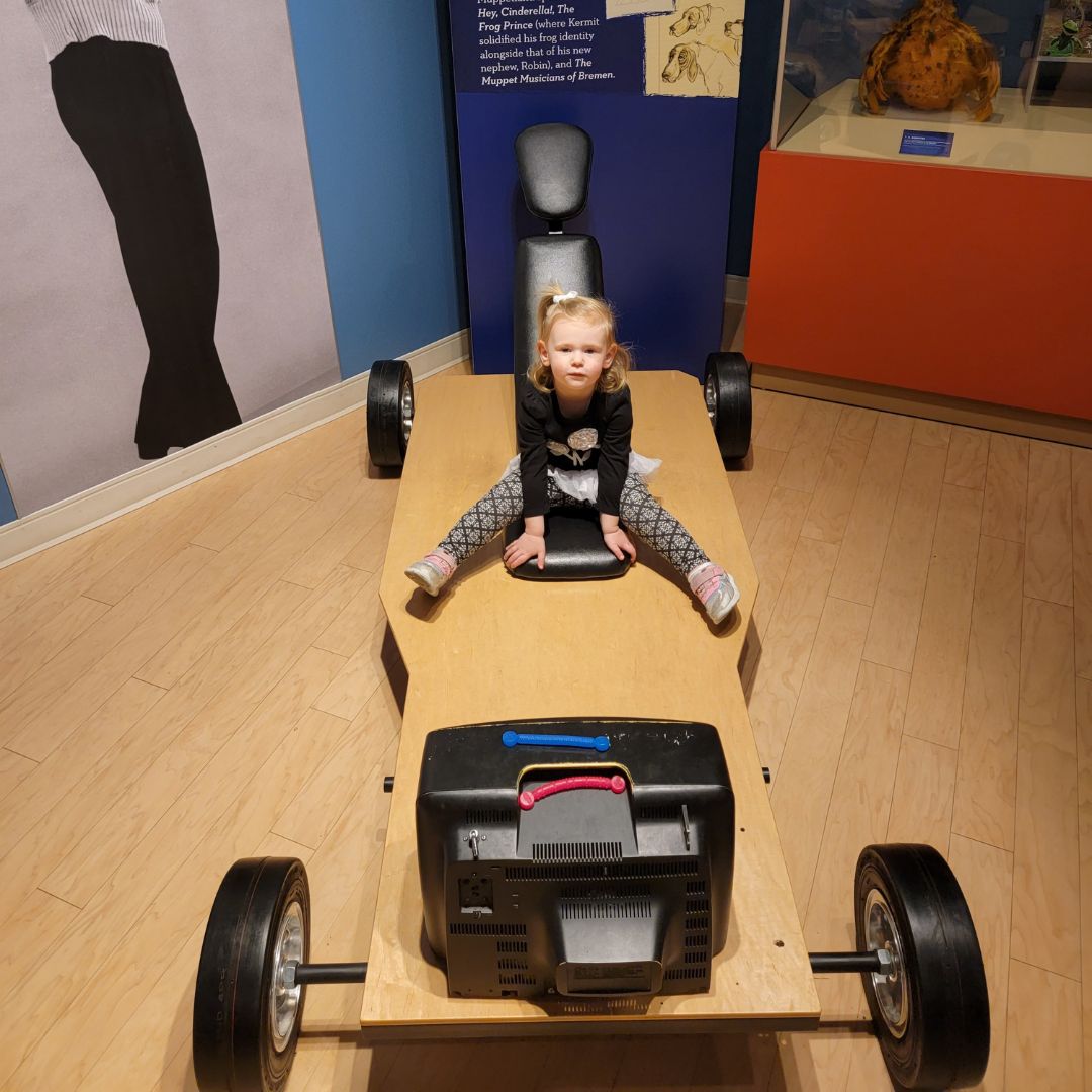 A young girl sits on top of a wooden car-like structure at the Center for Puppetry Arts in Atlanta.