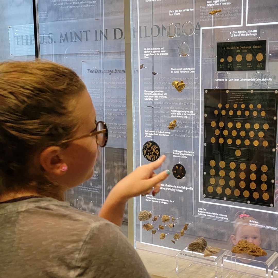 A preteen girl points toward a display of gold nuggets at the Dahlonega Gold Museum.