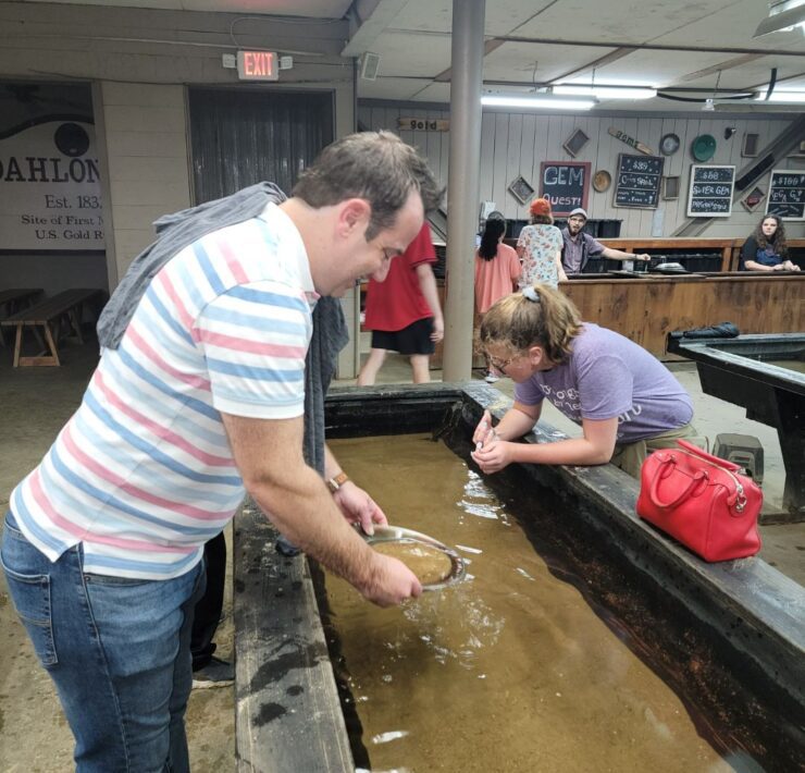 A man in a pink and blue striped shirt and a preteen girl in purple pan for gold at the Consolidated Gold Mine in Cleveland, GA.