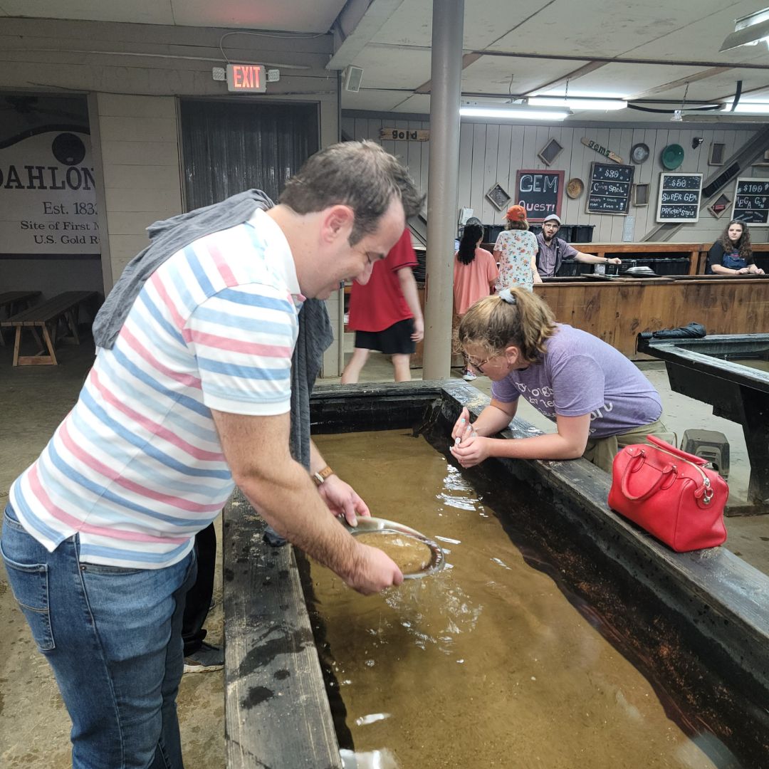 A man in a pink and blue striped shirt and a preteen girl in purple pan for gold at the Consolidated Gold Mine in Cleveland, GA.