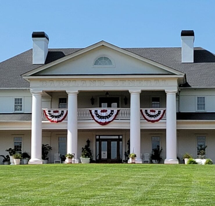 The exterior of the BabyLand General Hospital in Dahlonega can be seen with 4 large white columns and a large balcony with red, white, and blue patriotic banners hanging.
