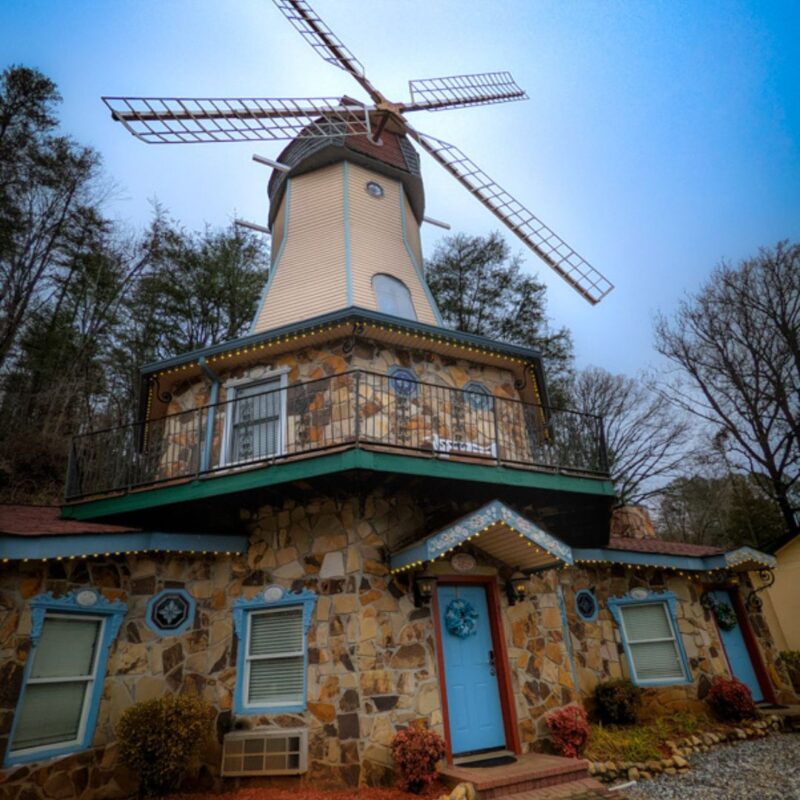 A windmill on the base of a rock-covered building stands proudly with trees behind it. 