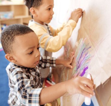 Two young children color on a piece of cardboard at a parents' night out.